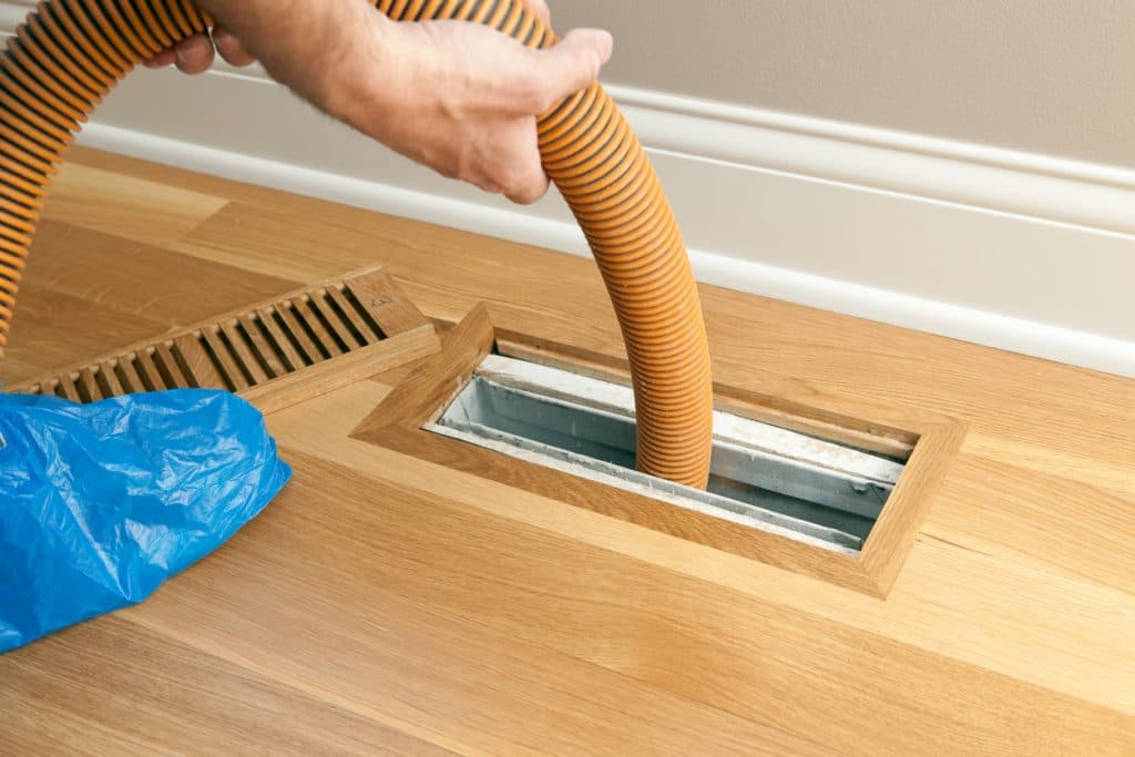 Vent Pro NYC technician feeding a cleaning hose into a hardwood floor vent to clear the accessible duct run