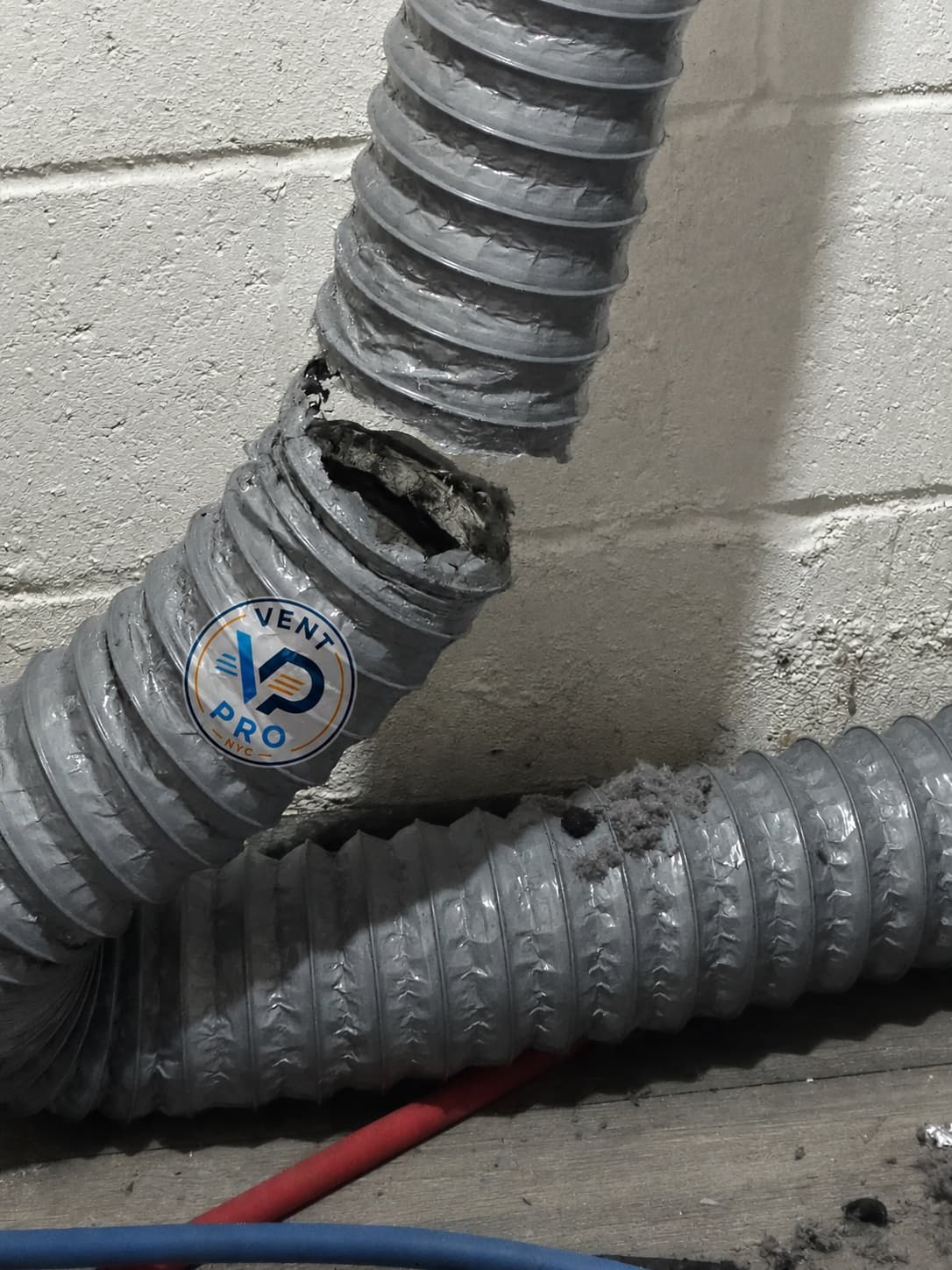 A cracked, split dryer duct packed with lint where it tore apart from the wall — the kind of unsafe hose Vent Pro NYC replaces
