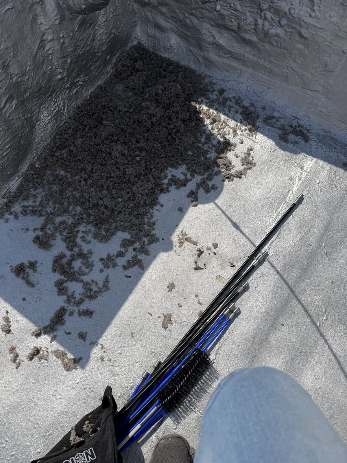 Flexible cleaning rods and a vent brush laid on a brownstone roof beside lint pulled from the dryer vent line