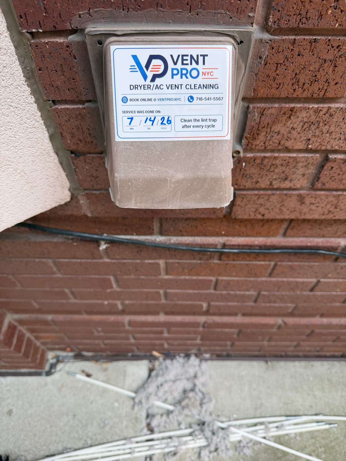 A Vent Pro NYC service tag dated 7/14/26 on a freshly cleaned exterior dryer vent on a Brooklyn brick wall, with the lint pulled from the line piled on the pavement below