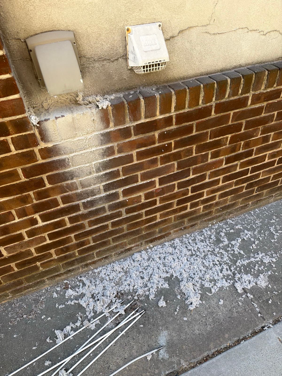 Two exterior dryer vent covers on a brick wall with lint cleared onto the pavement below