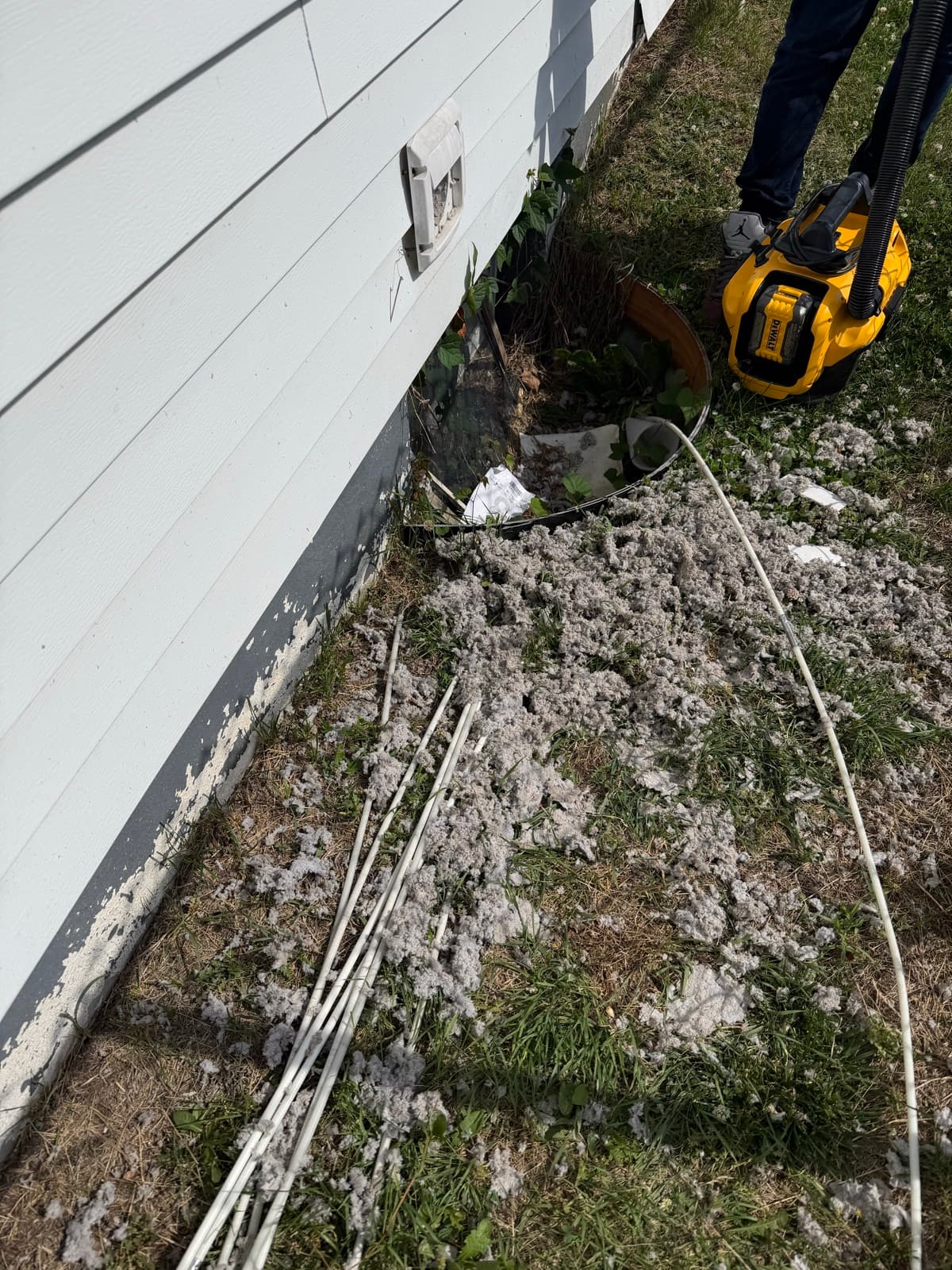 Vent Pro NYC clearing an exterior wall dryer vent with a vacuum, a pile of removed lint on the ground