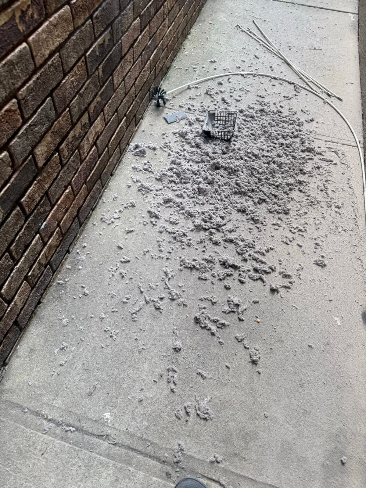 A wide spread of grey lint removed from a dryer vent, with cleaning rods and brush on the pavement