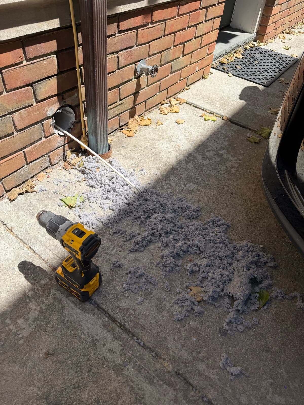 Vent Pro NYC running a rotary brush on a drill into an exterior wall dryer vent, lint expelled onto the ground