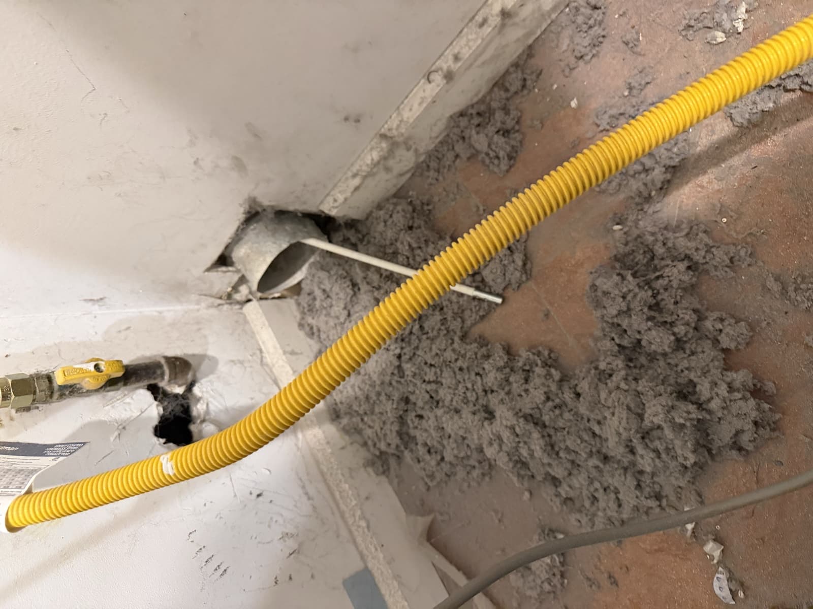A thick pile of lint pulled out of a wall dryer duct onto the floor behind the machine in a Brooklyn home